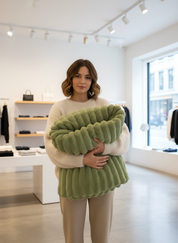 Green knitted blanket with ribbed texture held by model in store setting