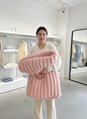 Pink knitted blanket with ribbed texture held by model in store setting