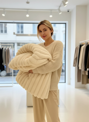 Beige knitted blanket with ribbed texture held by model in store setting