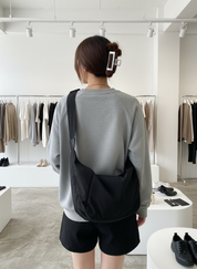 Woman wearing black shoulder bag with gray sweatshirt and black shorts, back view