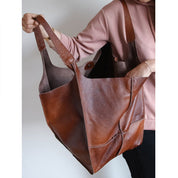 Brown slouchy tote with large exterior pockets, front view with hand inside