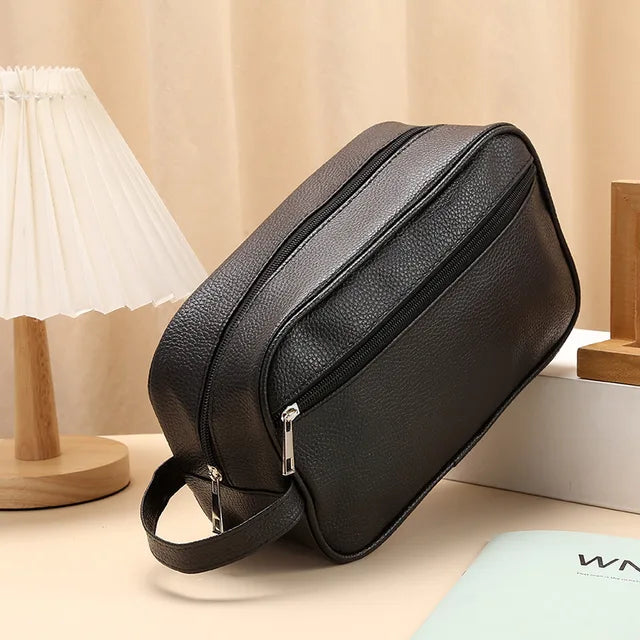 Black toiletry bag on table with lamp and book