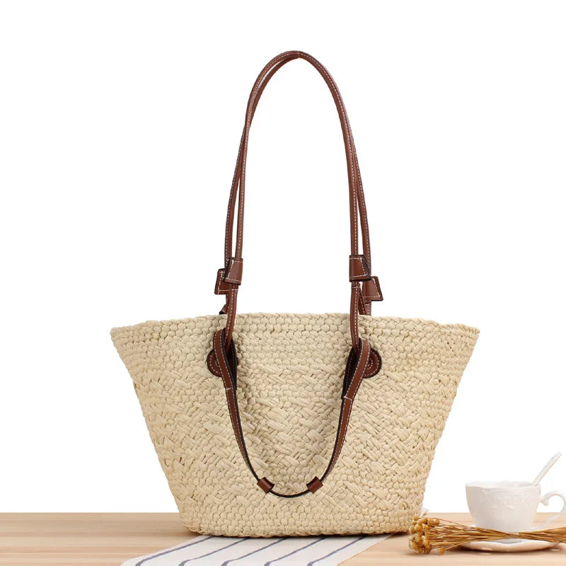 Woven straw tote bag with brown leather accents front view on striped cloth