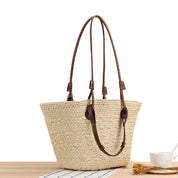 Woven straw tote bag with brown leather accents front view on wooden table