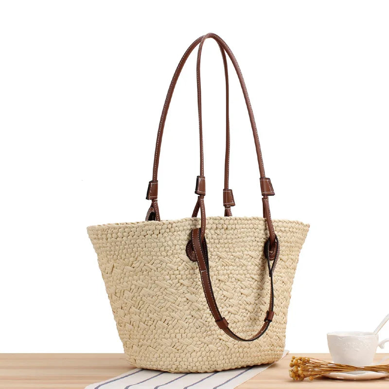 Woven straw tote bag with brown leather accents front view on wooden table