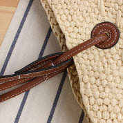 Close-up of woven straw tote bag handle with brown leather accent