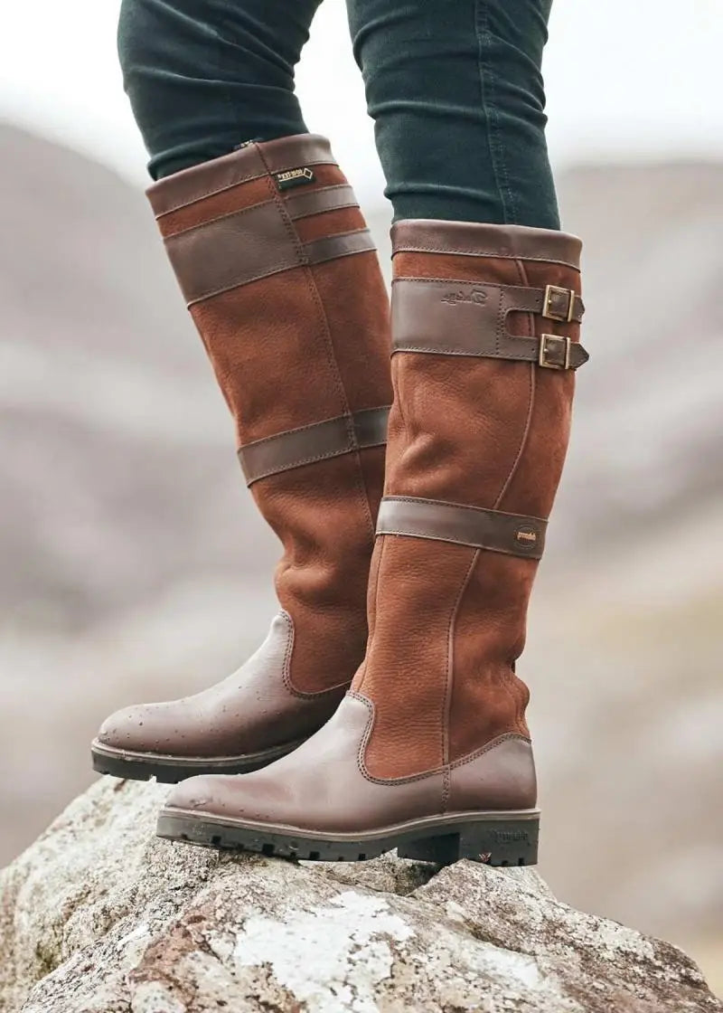 Tan leather knee-high boots with buckle detail, worn on rock