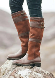 Tan leather knee-high boots with buckle detail, worn on rock