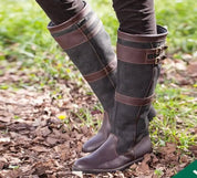 Brown leather knee-high boots with buckle detail, worn on grass