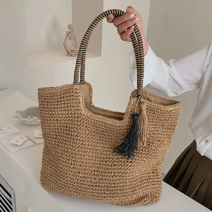Woven straw tote bag with tassel, held by hand, side view