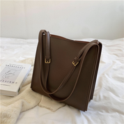 Brown leather shoulder bag on bed with book
